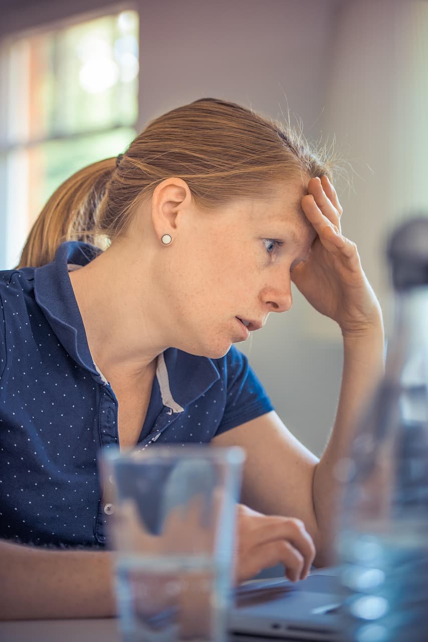 A person at her laptop with her head resting in her hand, working through something difficult