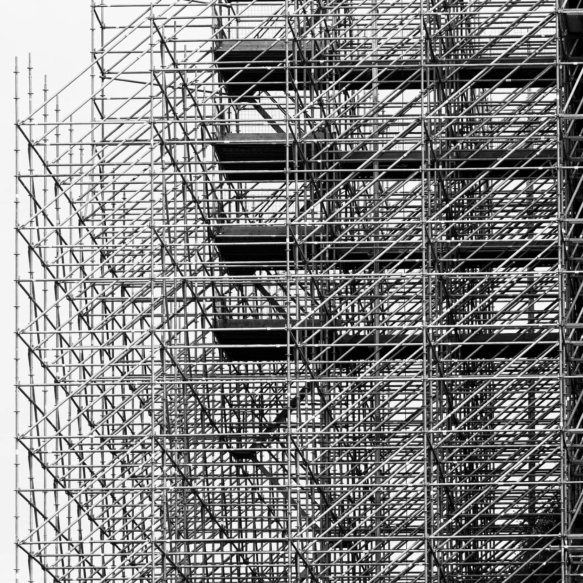 Black-and-white photo of dense construction scaffolding rising against a pale sky