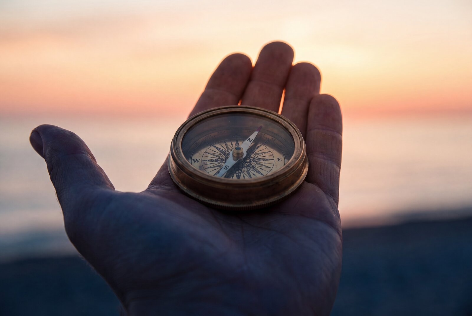 A hand cradling a compass at sunset — the human setting the course through a high-tech world.