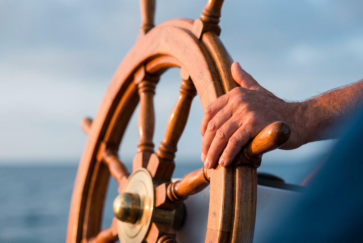 A weathered hand grips the polished wooden spoke of a ship's helm at sea — the human setting the course.